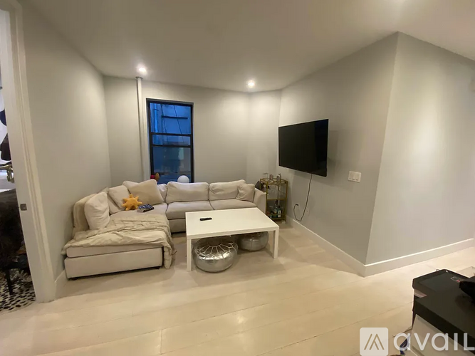A living room with a white couch, a white coffee table, and a flat screen TV mounted on the wall.