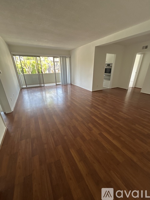 A spacious room with wooden flooring and a large window.