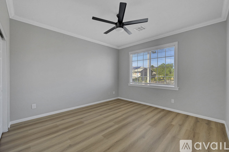 A room with a ceiling fan and a window overlooking a building.