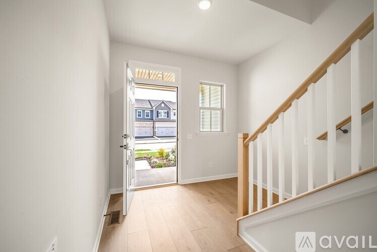 A white hallway with a wooden staircase and a doorway leading to a house.