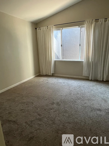 A room with a carpeted floor and a window with curtains.