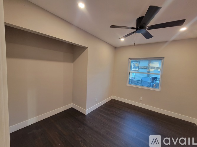 A room with a ceiling fan and a window showing a view of a fence and a building.