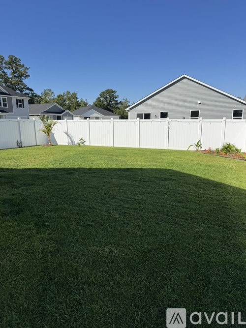 A backyard with a white fence and a grey house.