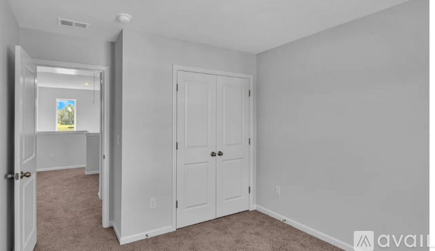 A room with a white door and a window with a view of trees.