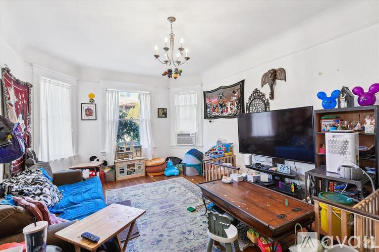 A cluttered living room with a wooden table, a television, and a chandelier.