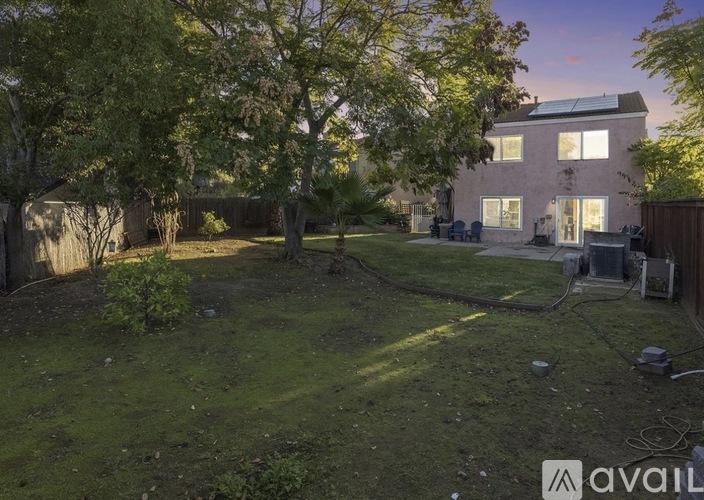A backyard with a tree, a fence, and a house with solar panels on the roof.