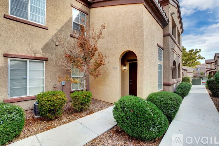 A beige building with a brown door and windows with bushes in front.