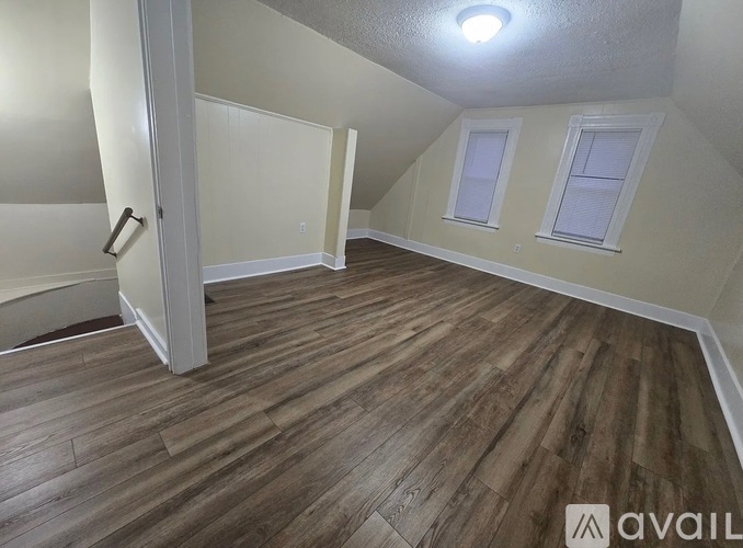 A room with wooden flooring and two windows.