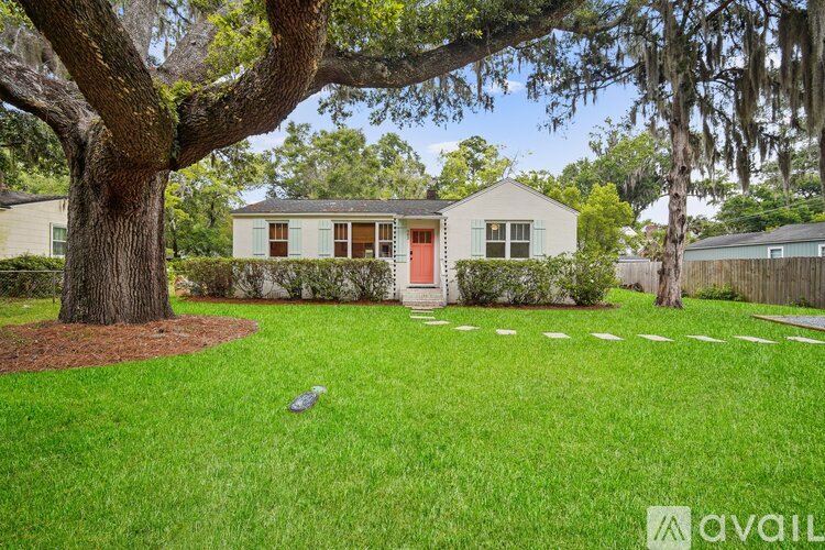 A house with a red door is surrounded by a well-manicured lawn and trees.