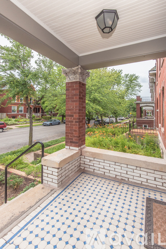 A porch with a brick column and a tiled floor.