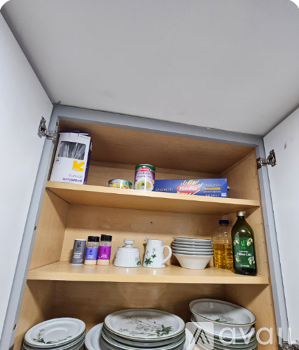 A kitchen cabinet is open, revealing plates, bowls, and a box of cereal.