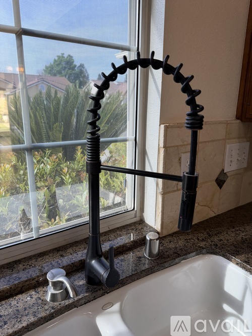 A bathroom sink with a black faucet and a window showing a view of a house and trees.