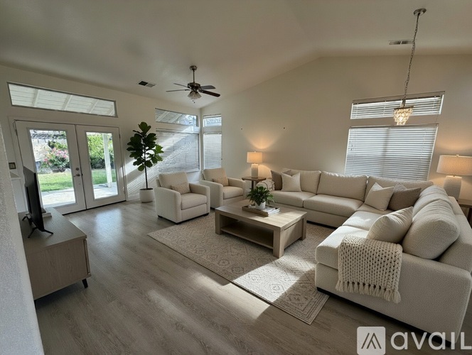 A spacious living room with white furniture and a flat-screen TV.