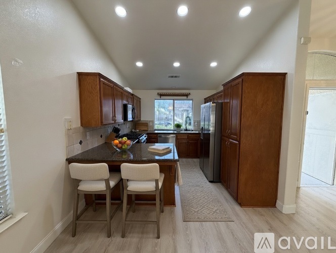 A kitchen with brown cabinets and a dark countertop with two chairs.