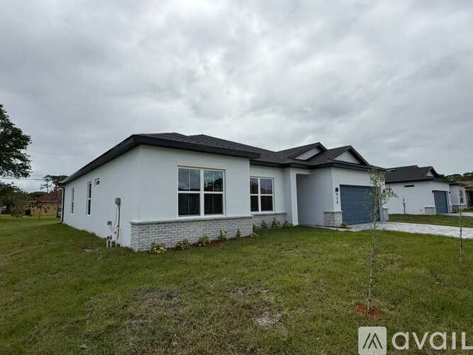 A house with a grey roof and a white exterior is surrounded by a grassy area.