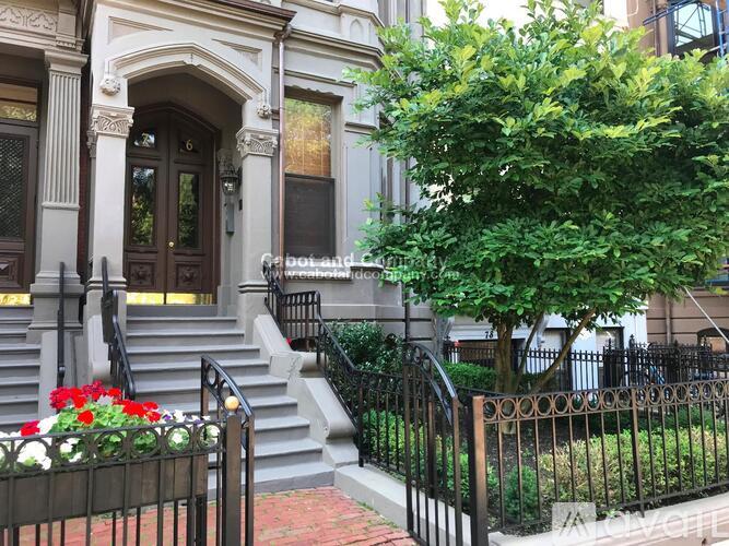 A black wrought iron fence surrounds a brick walkway leading to a large, ornate front door.