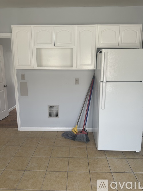 A white fridge in a kitchen with a broom and a mop.