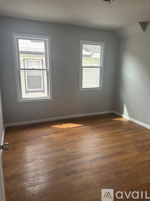 A room with wooden flooring and two windows.