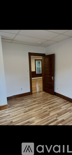 A room with wooden flooring and a white wall with a doorway leading to another room.