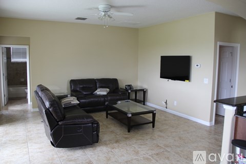 A living room with a black leather couch and a flat screen TV mounted on the wall.