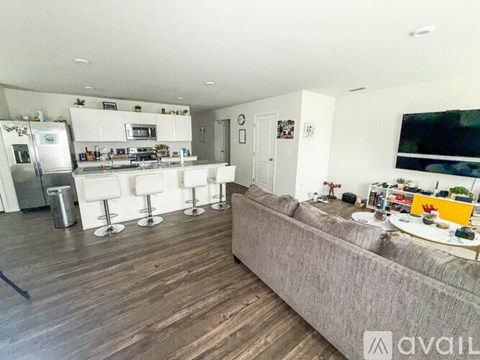 A living room with a grey couch and a kitchen area in the background.