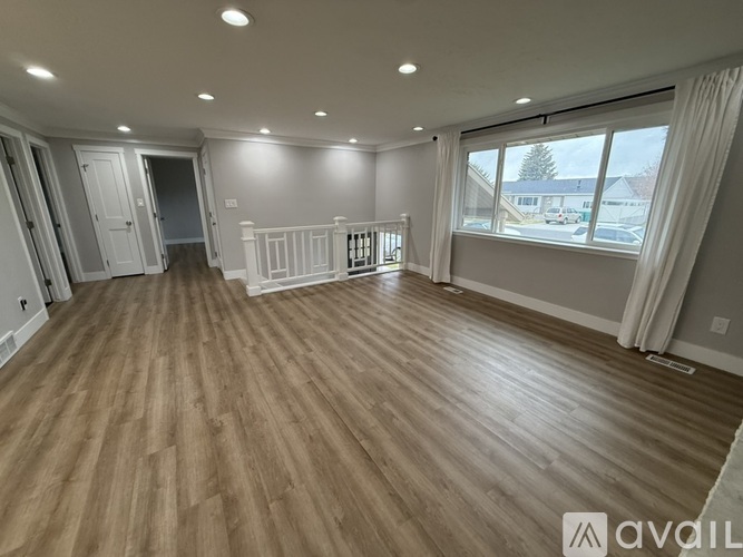A spacious room with wooden flooring and a large window with white curtains.