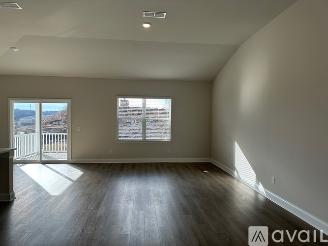 A spacious room with wooden floors and a large window overlooking a deck.