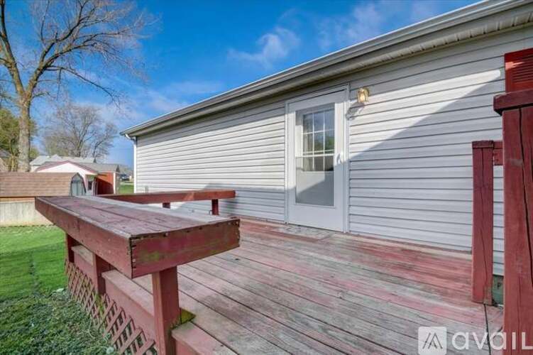A wooden deck with a bench is in front of a grey house.