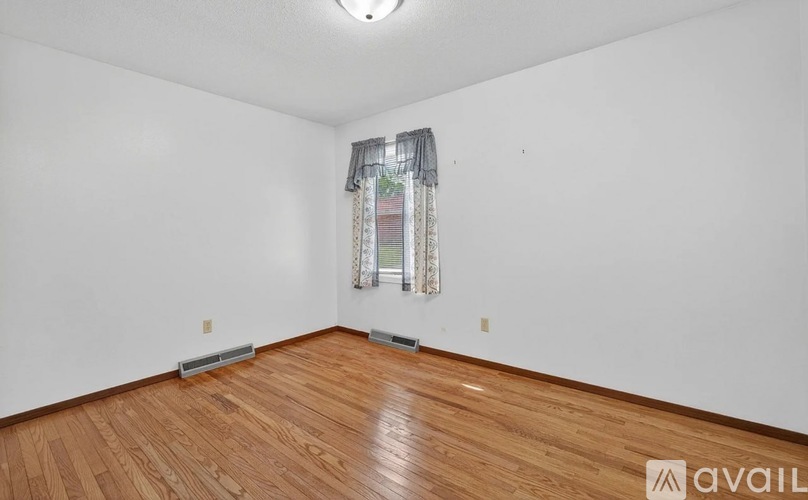 A room with wooden flooring and a window with a curtain.