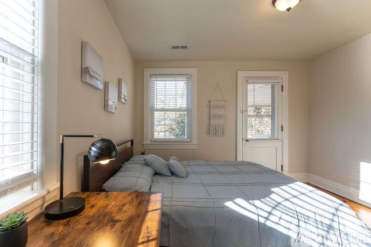 A bedroom with a bed, a nightstand with a lamp, and a window with blinds.