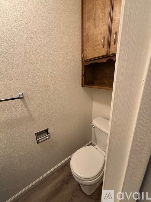 A white toilet in a small bathroom with a wooden cabinet above it.