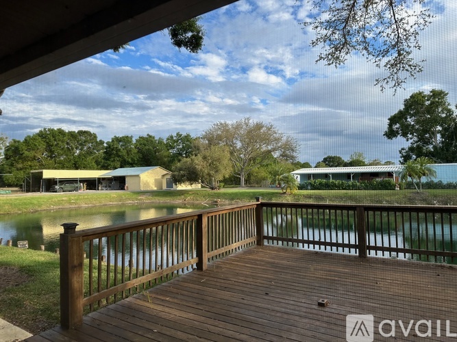 A wooden deck overlooks a body of water with a house and trees in the background.