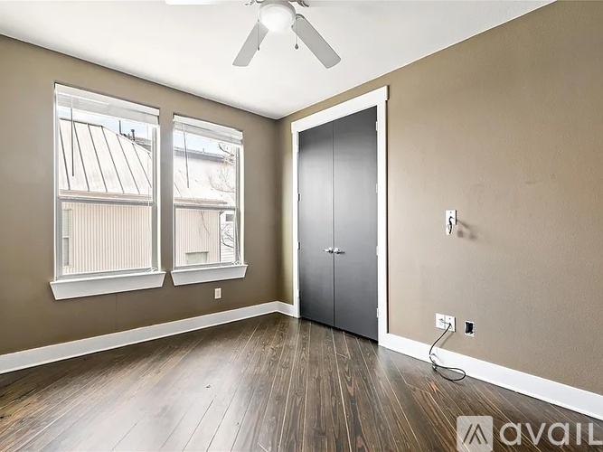 A room with a ceiling fan, two windows, and a door.