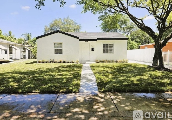 A white house with a black roof is surrounded by a well-manicured lawn and trees.