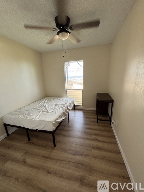 A bedroom with a bed, a desk, and a ceiling fan.