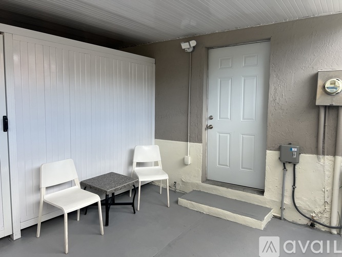 A room with a white door, two white chairs and a table.
