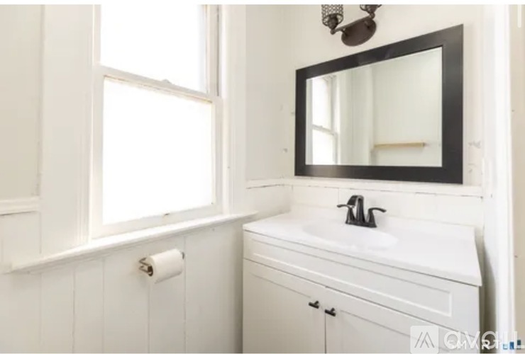 A white bathroom with a sink, mirror, and a window.