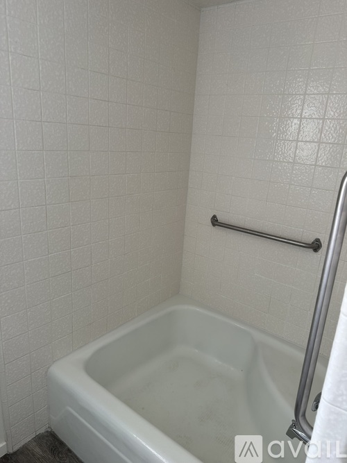 A white tiled bathroom with a white tub and a silver grab bar.