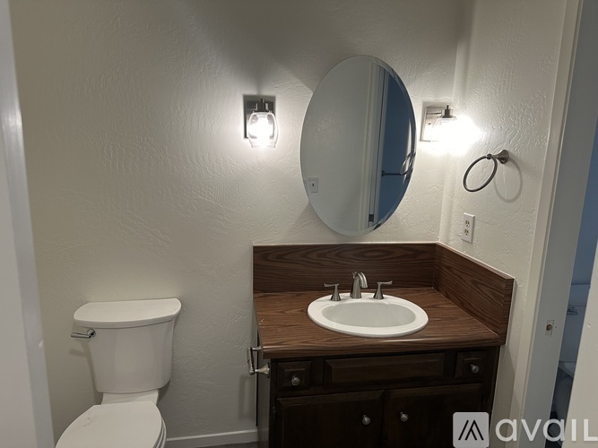 A bathroom with a toilet, sink, mirror, and lights.