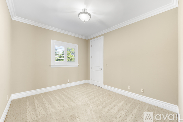 A room with beige walls and carpeting, a window with a view of trees, and a door.
