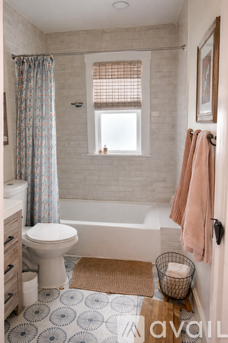 A bathroom with a toilet, a bathtub, a window, and a rug.