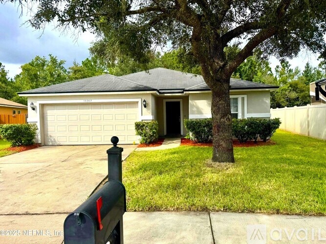A white house with a grey garage door is surrounded by a green lawn and trees.