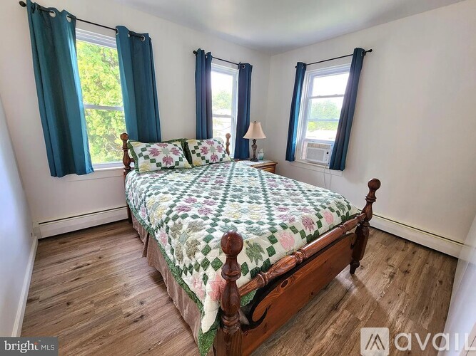 A bedroom with a bed, wooden floors, and windows with blue curtains.