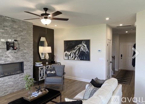 A living room with a fireplace, a grey armchair, a white sofa, and a painting of a horse.