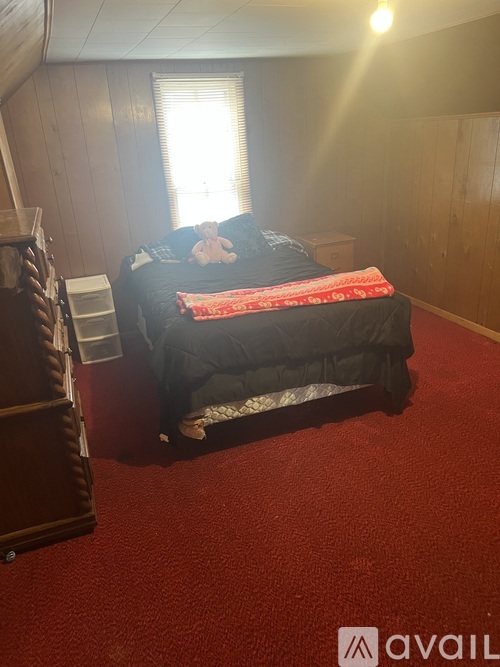 A bed with a red blanket is in a room with wooden walls.