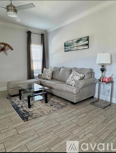 A living room with a grey couch, a glass table, and a rug.