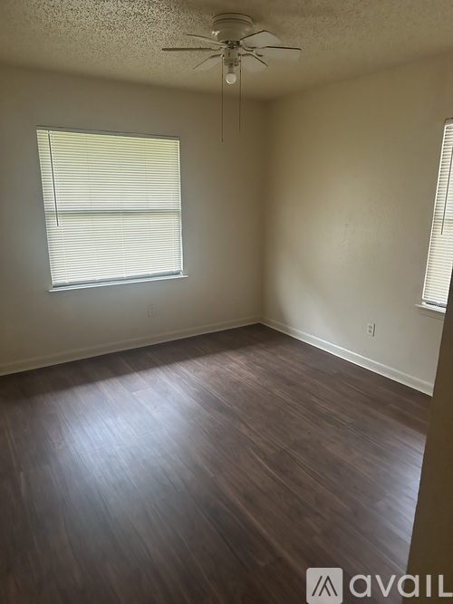 A room with a ceiling fan and light, wooden floors, and a window with blinds.