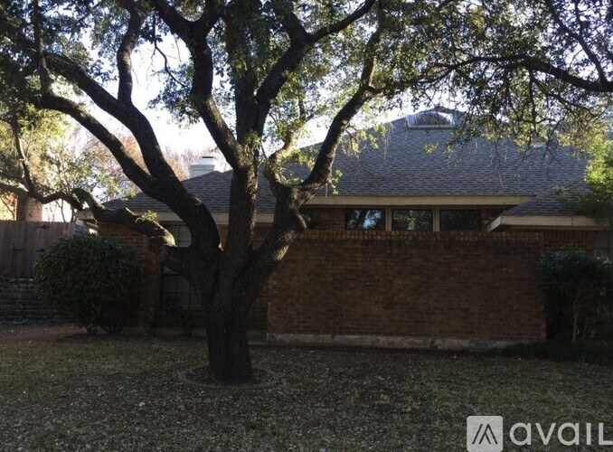 A tree in front of a house with a roof.