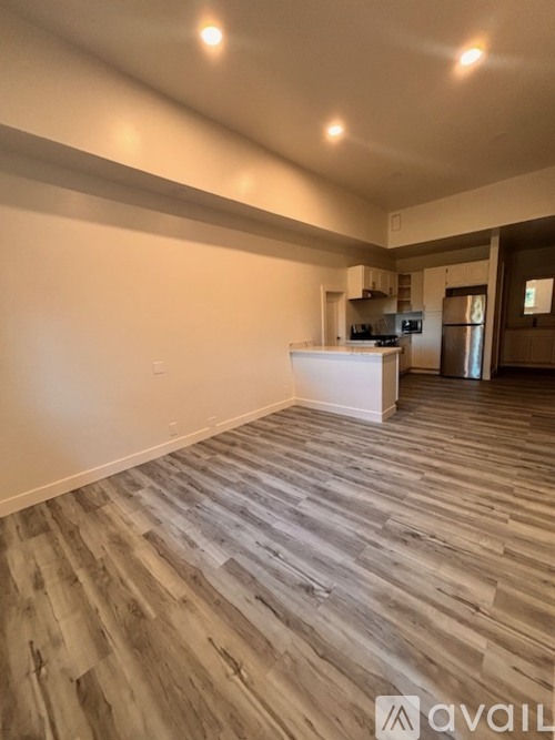 A spacious room with wooden flooring and a kitchen area in the background.