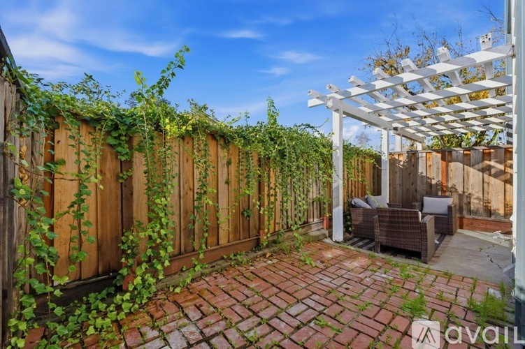 A patio with a white pergola and a wooden fence covered in green vines.